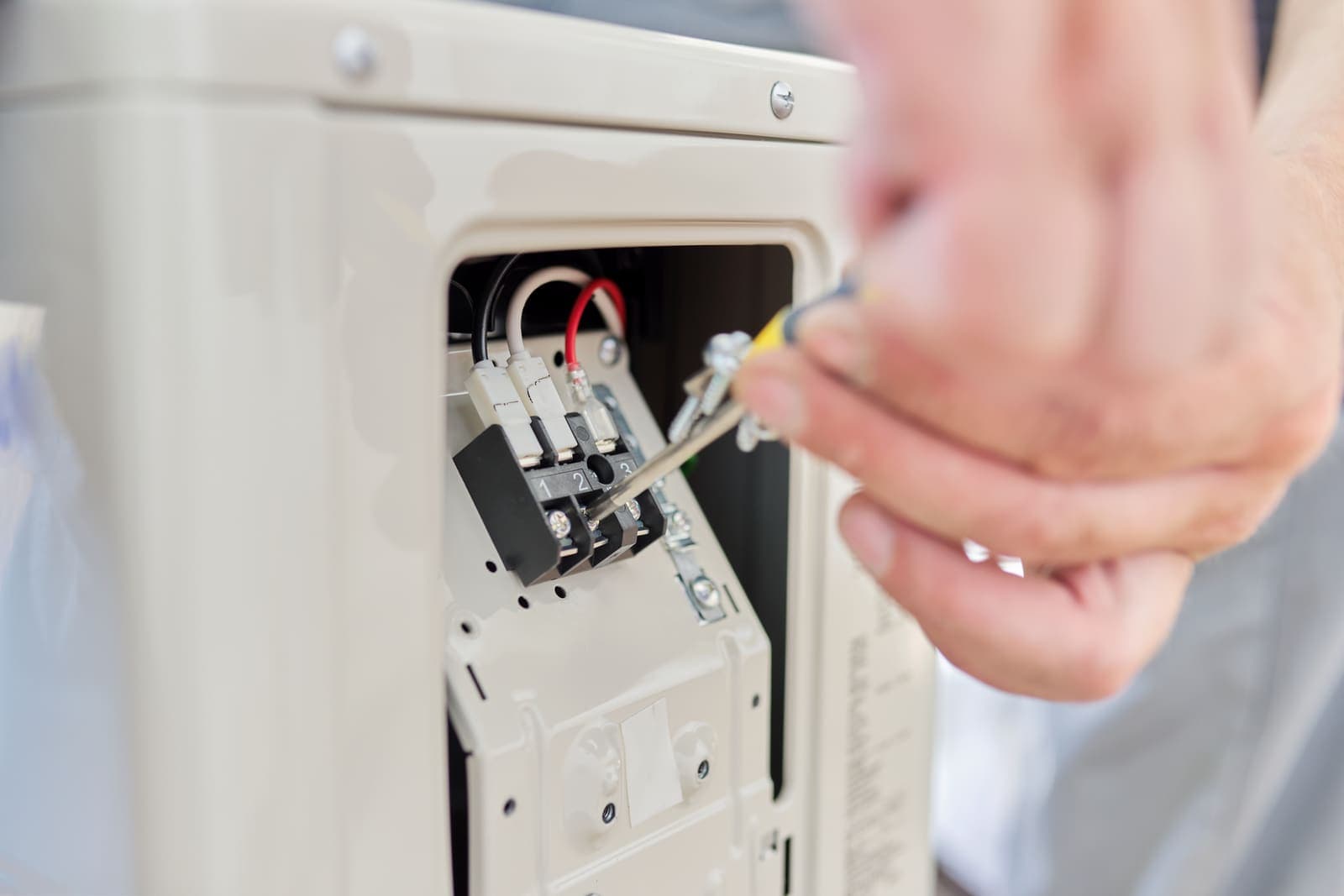 A technician's hands working on the electrical components inside an air conditioner