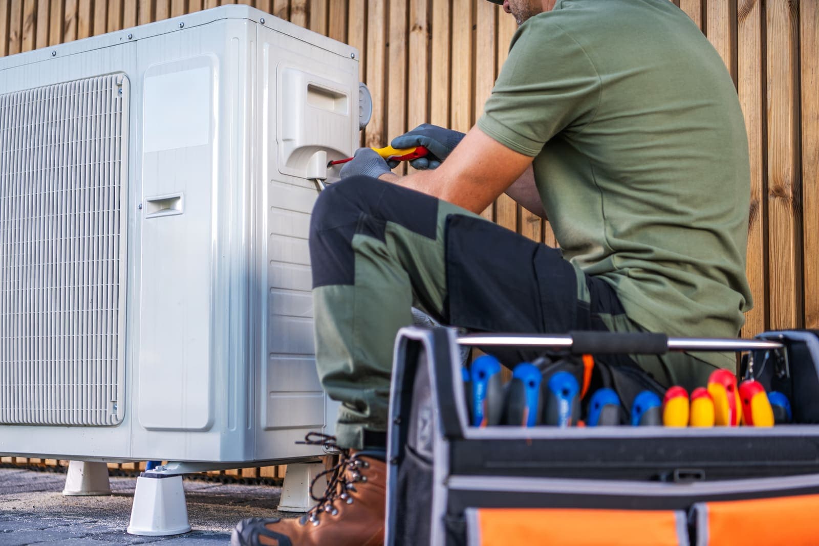 An HVAC technician servicing an outdoor air conditioning condenser unit