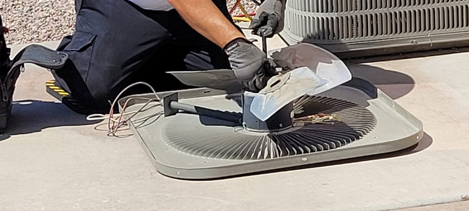 A repairman servicing the fan of an outdoor air conditioner unit