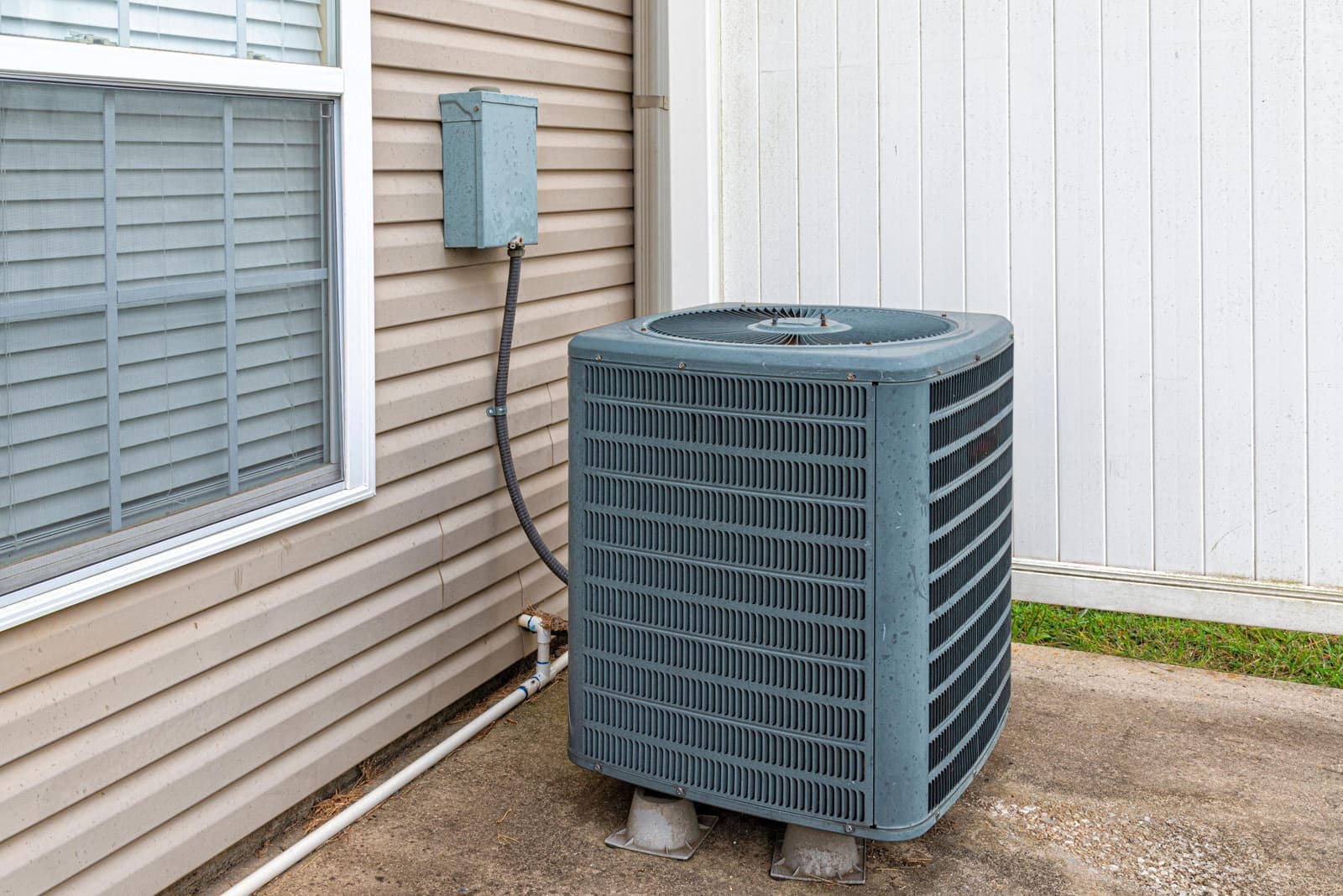 A residential air conditioning condenser unit on a concrete slab beside a home