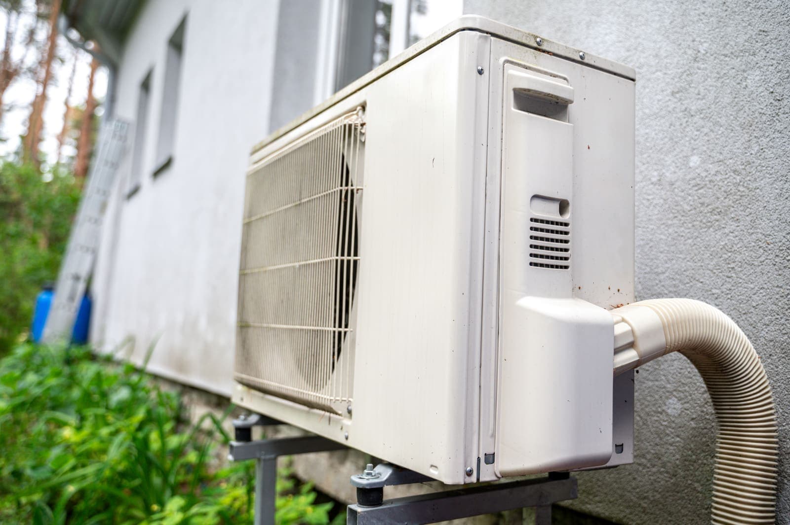 An outdoor air conditioning unit beside a house surrounded by greenery