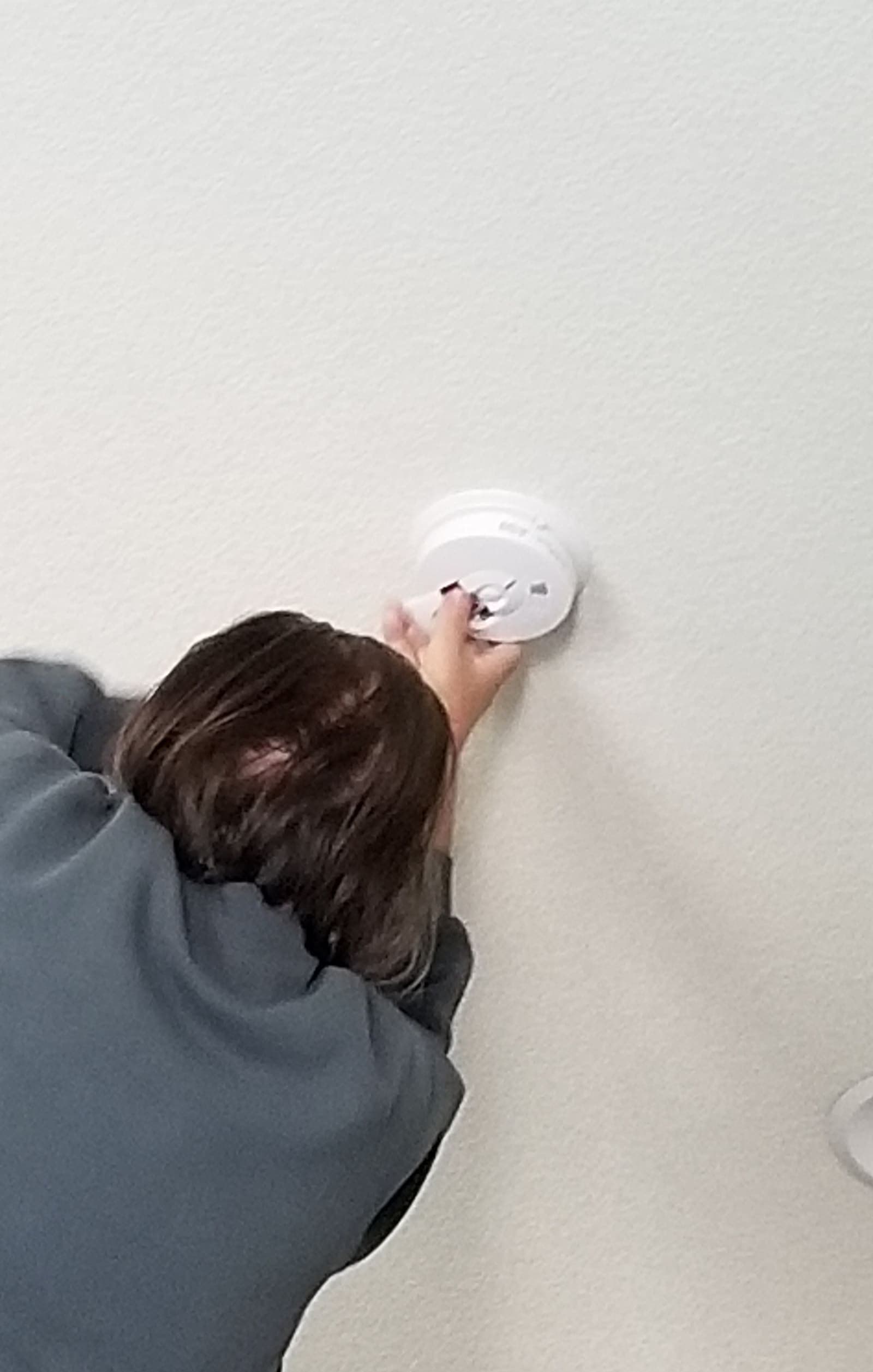 An adult checking a ceiling-mounted safety detector in a home