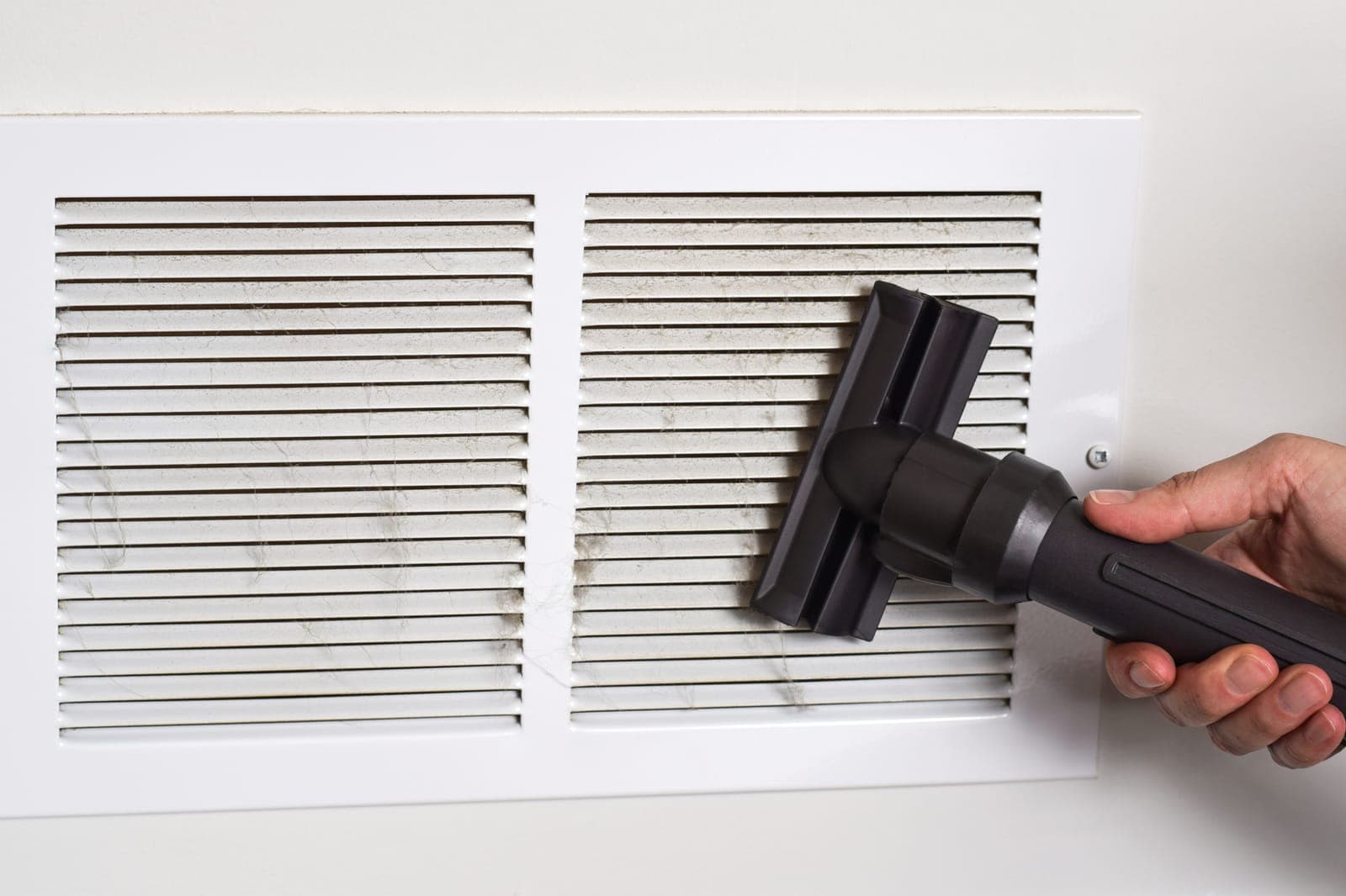 A vacuum attachment cleaning dust from a white air vent