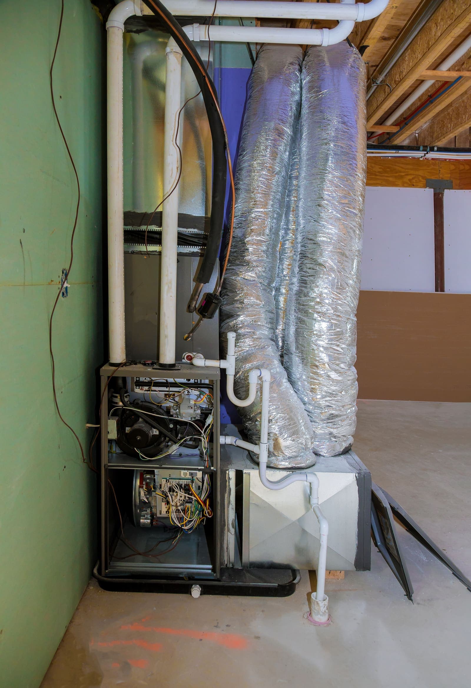An indoor HVAC air handler with insulated ductwork and pipes in an unfinished space