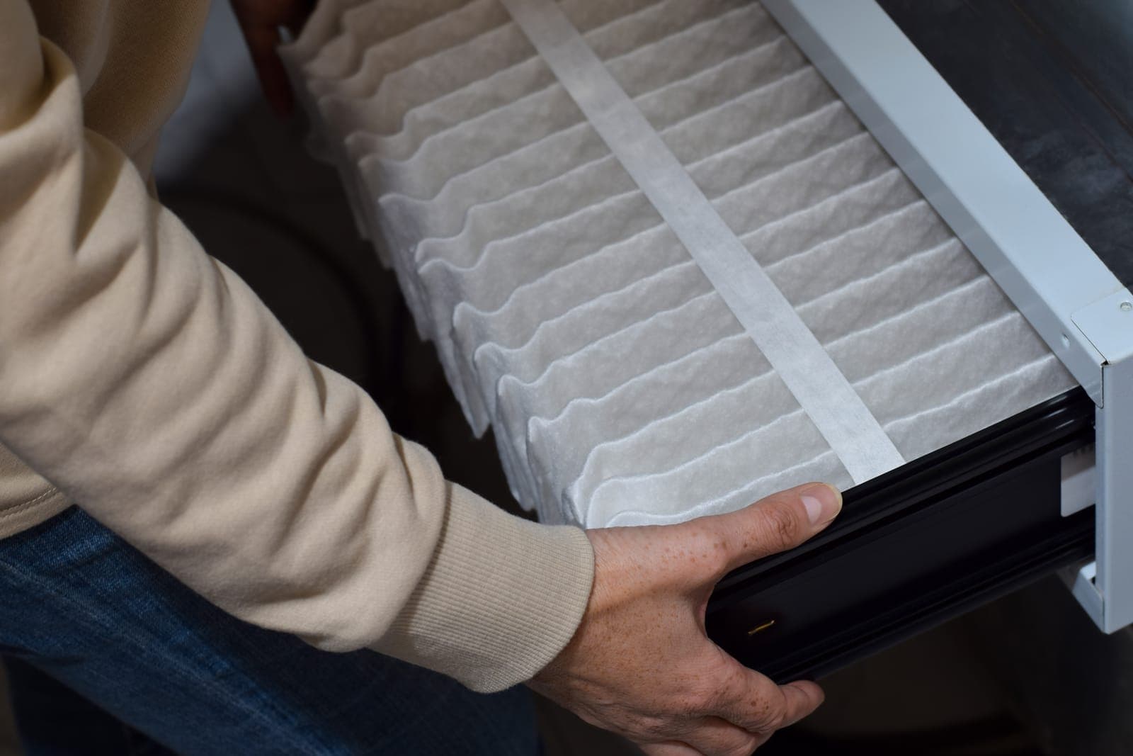 Hands sliding a clean pleated air filter into an HVAC unit