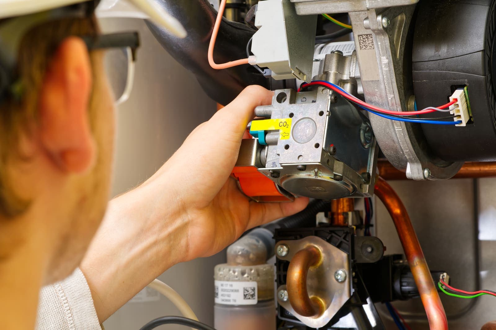 A repair technician working on the gas valve and wiring inside a home furnace