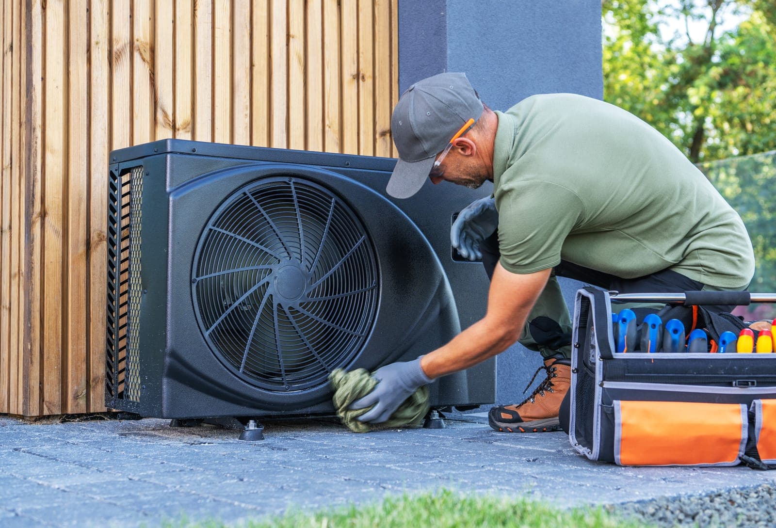 A technician cleaning and maintaining a modern heat pump outside a home