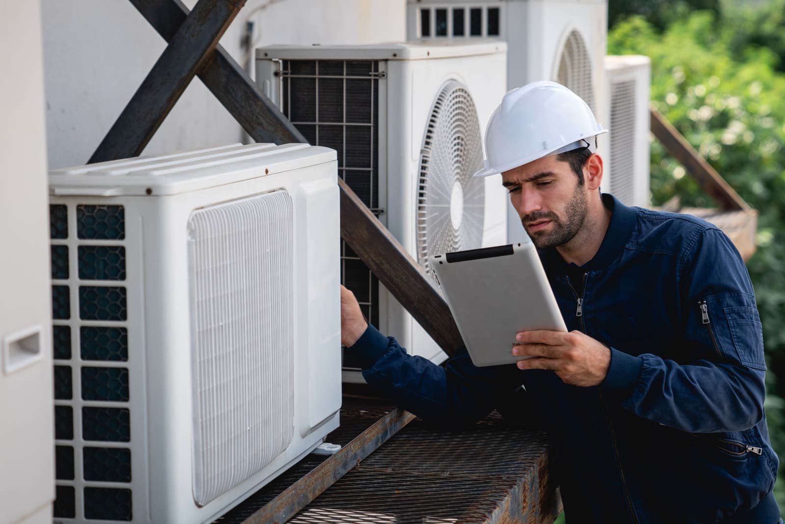 An HVAC technician in a hard hat inspecting outdoor units