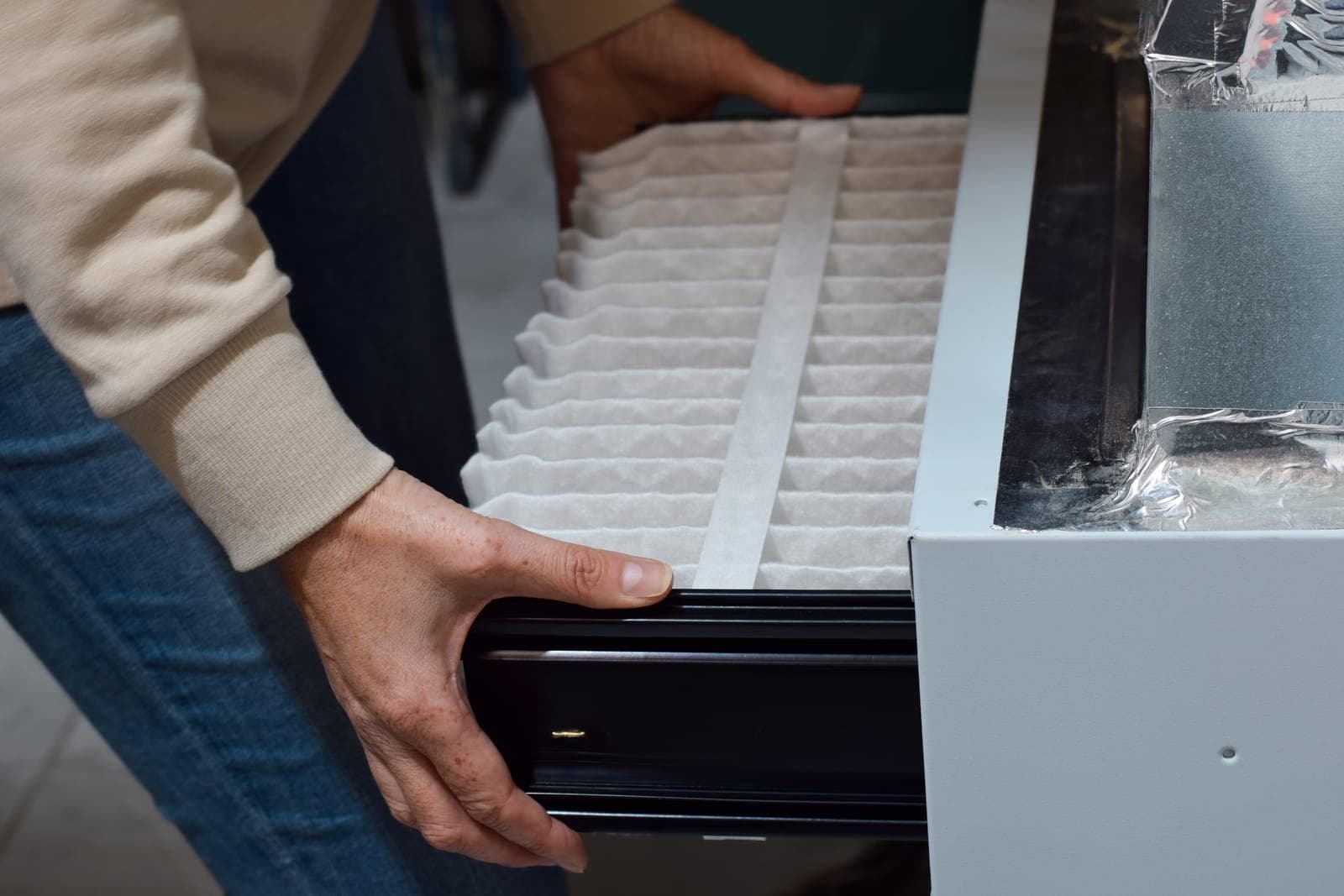 A homeowner sliding a clean pleated air filter into an HVAC return