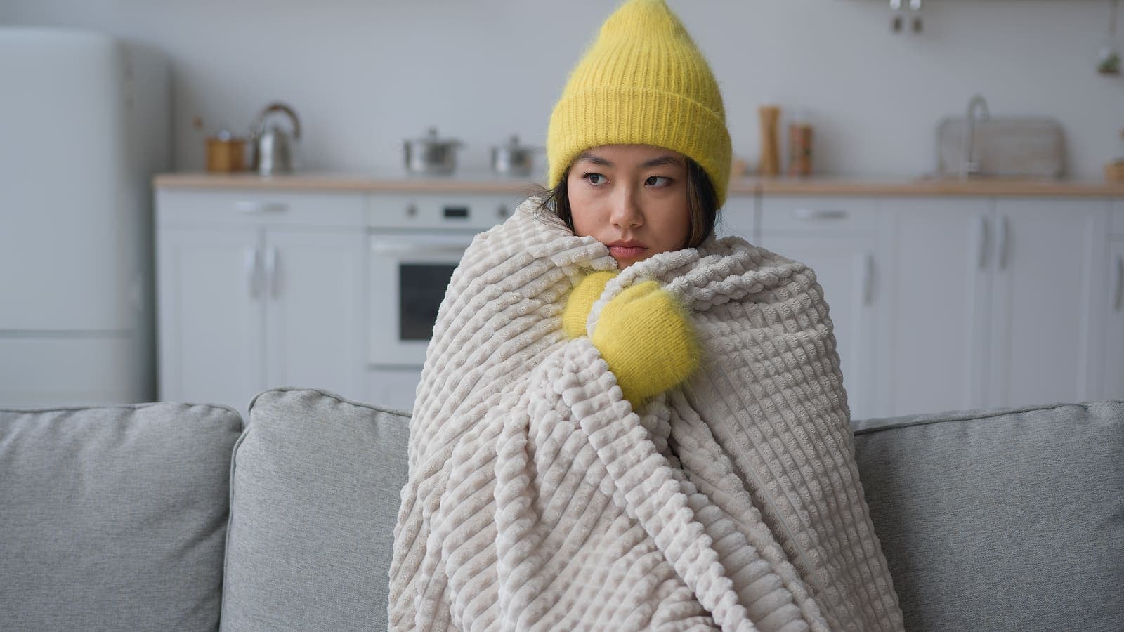 A woman wrapped in a blanket feeling cold inside her home