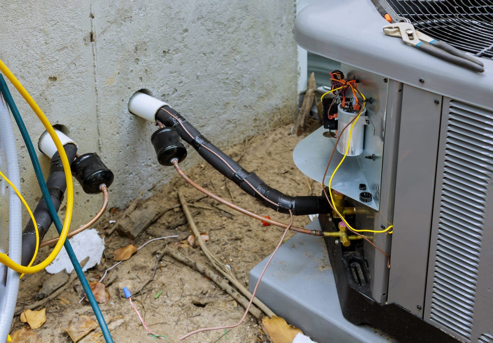 The drain and refrigerant piping connections at an outdoor HVAC unit