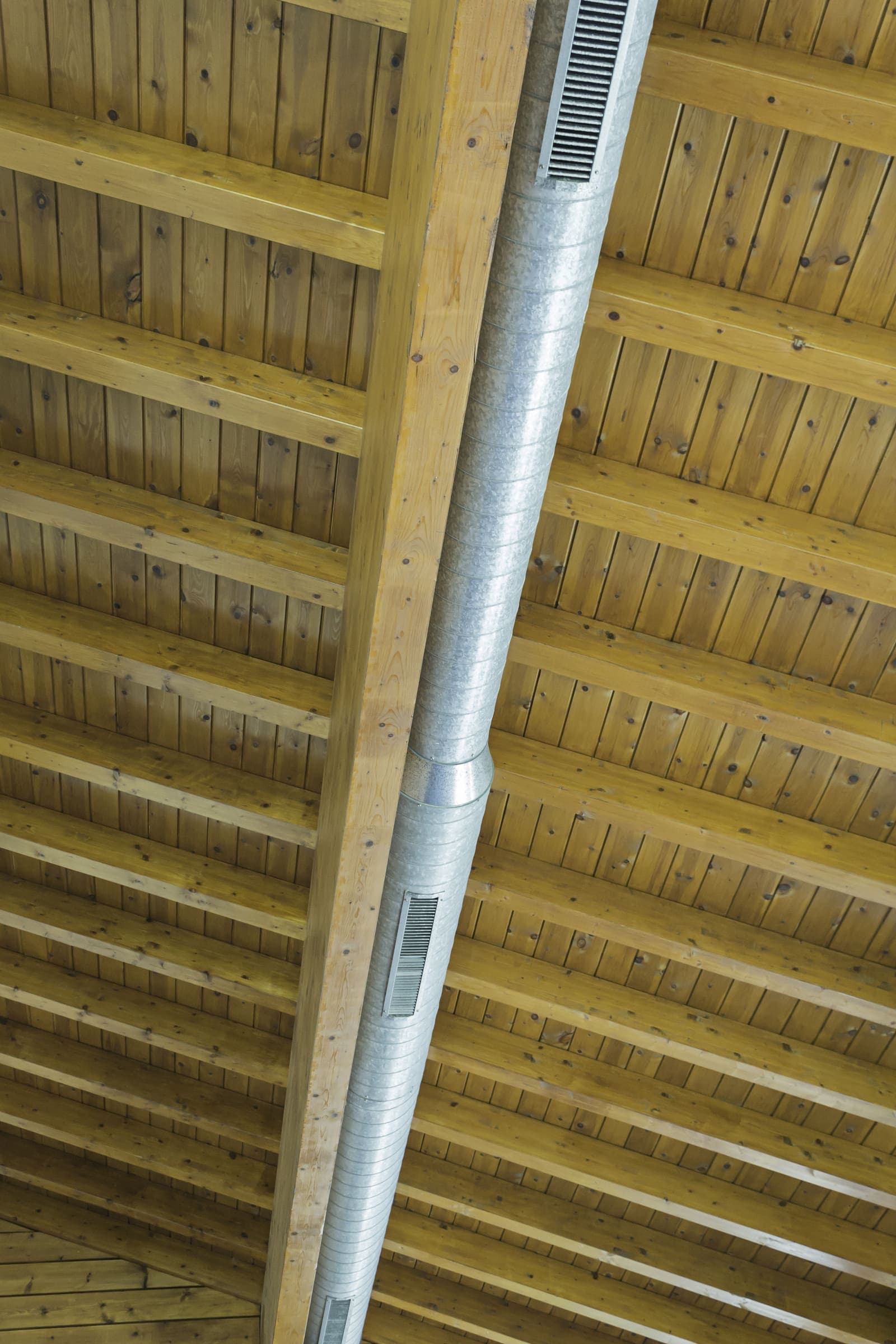 Metal HVAC ductwork running along a wooden ceiling structure