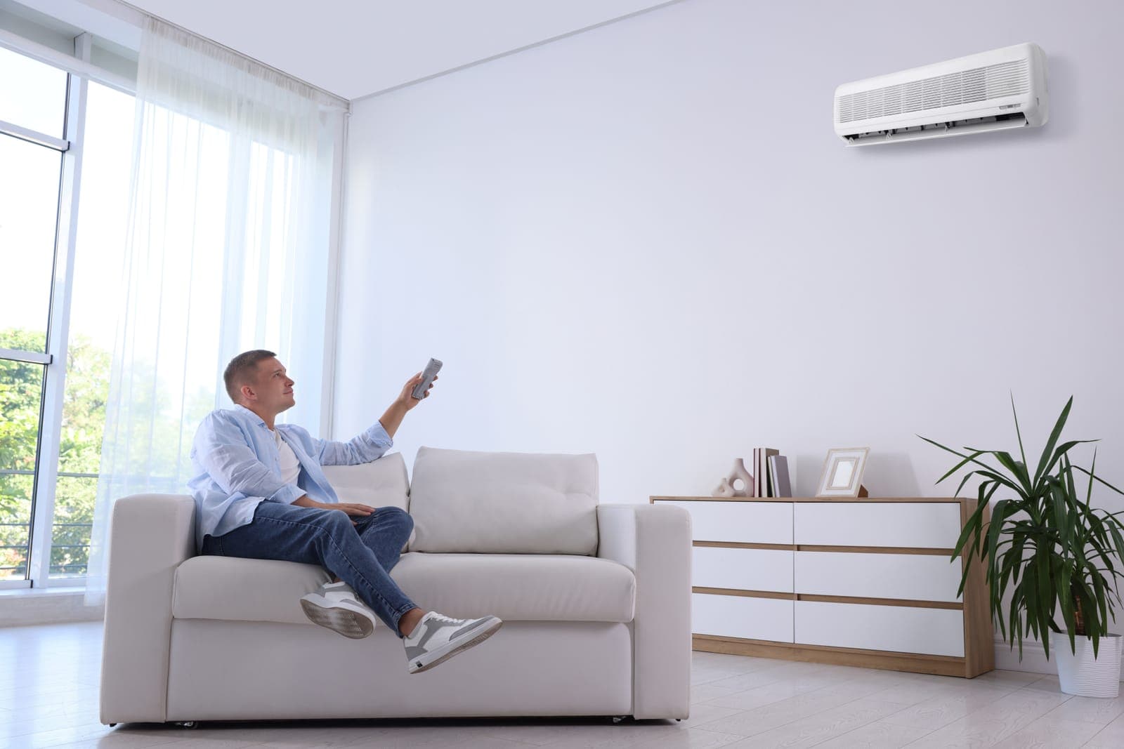 A man using a remote to adjust a wall-mounted ductless mini split in a bright living room