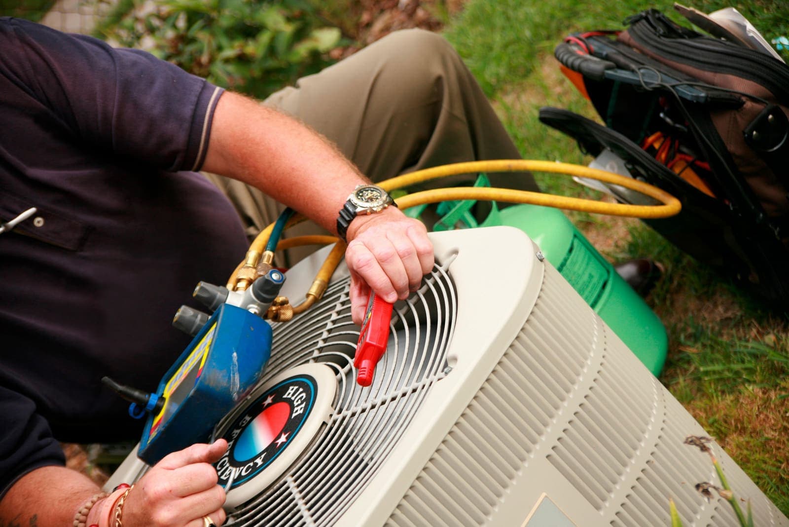 A technician connecting refrigerant manifold gauges to an outdoor air conditioning unit