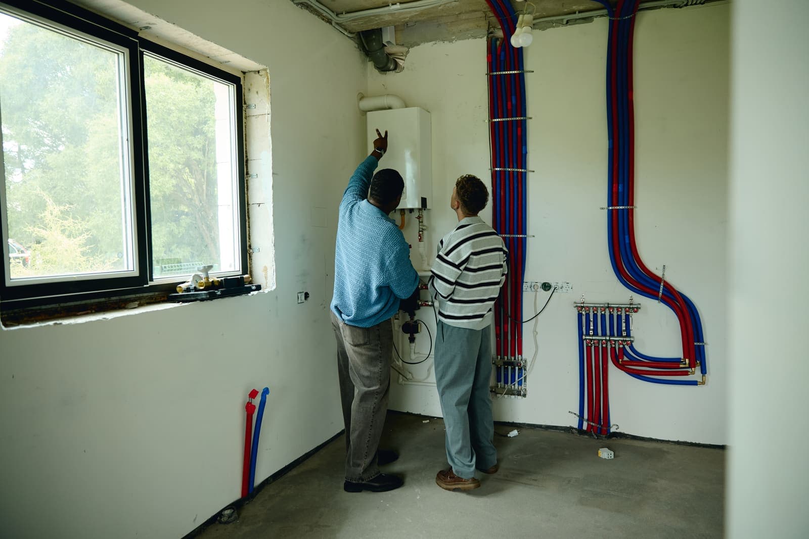 Two men inspecting a heating system in an unfinished basement room