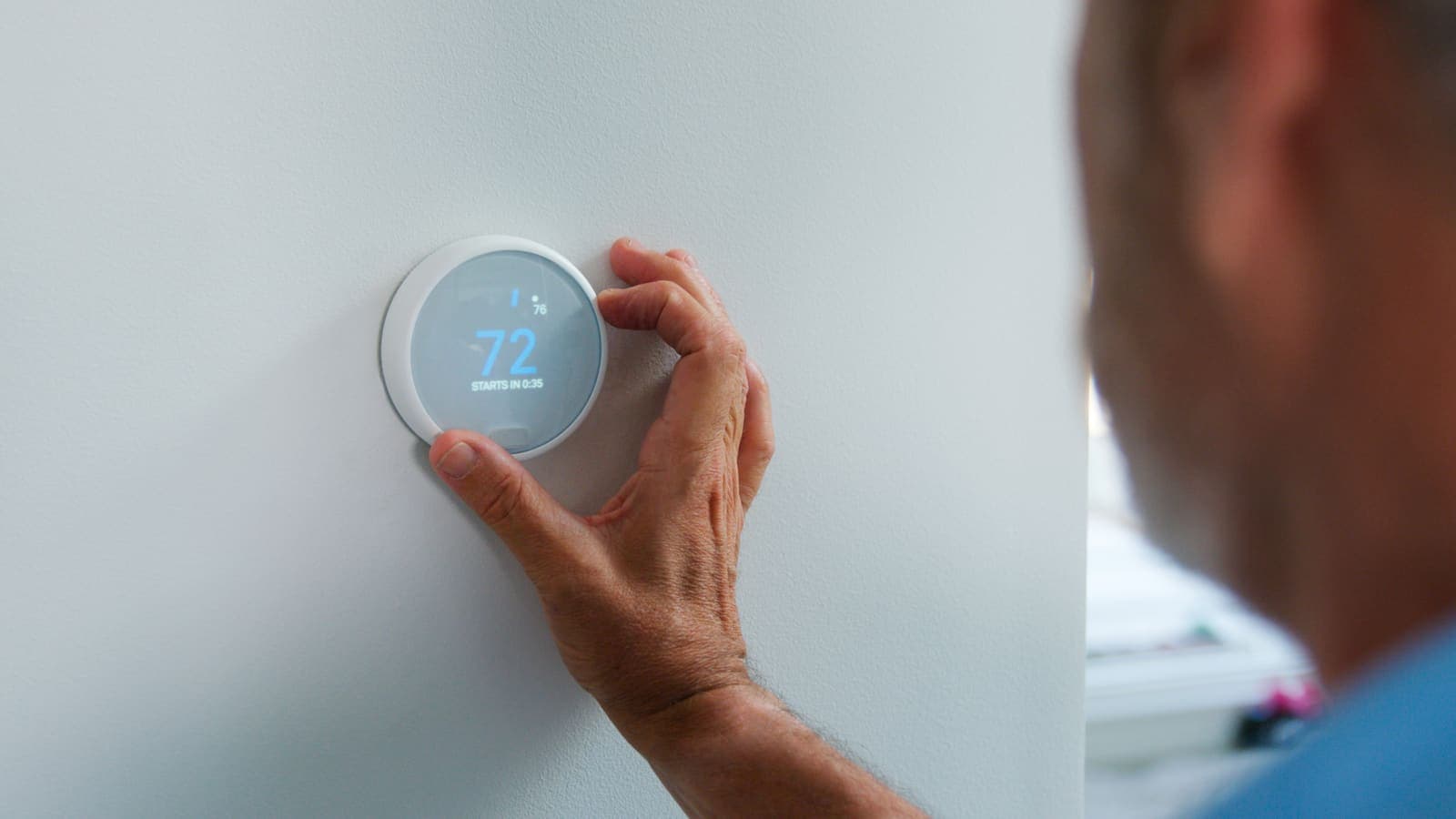 A hand adjusting a round smart thermostat in a home