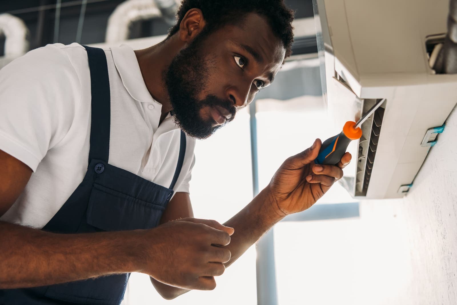 A technician repairing an air conditioner with a screwdriver